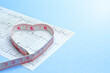 heart-shaped measuring tape and heart cardiogram. The concept of the harm of being overweight