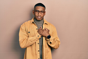 Wall Mural - Young black man wearing casual clothes and glasses smiling with hands on chest with closed eyes and grateful gesture on face. health concept.