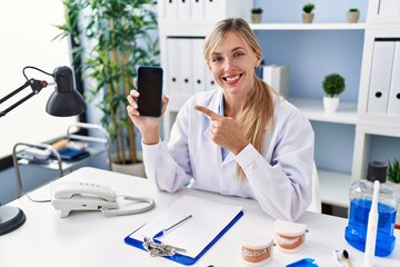 Poster - Beautiful dentist woman showing smartphone screen smiling happy pointing with hand and finger