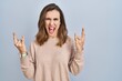 © Krakenimages.com - Young woman standing over isolated background shouting with crazy expression doing rock symbol with hands up. music star. heavy music concept.