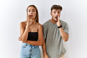 Wall Mural - Young beautiful couple standing together over isolated background hand on mouth telling secret rumor, whispering malicious talk conversation