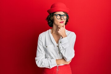 Poster - Young brunette woman wearing stewardess style and glasses serious face thinking about question with hand on chin, thoughtful about confusing idea