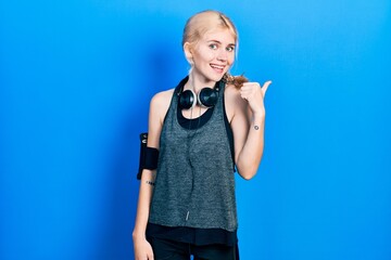 Canvas Print - Beautiful caucasian woman with blond hair wearing sportswear smiling with happy face looking and pointing to the side with thumb up.