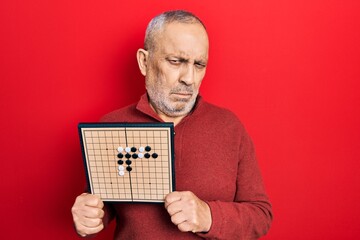 Sticker - Handsome mature man holding asian go game board depressed and worry for distress, crying angry and afraid. sad expression.