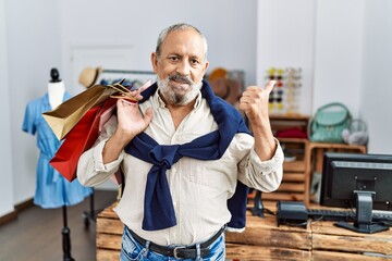 Poster - Handsome senior man holding shopping bags at boutique shop smiling happy and positive, thumb up doing excellent and approval sign