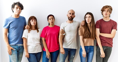 Wall Mural - Group of young friends standing together over isolated background making fish face with lips, crazy and comical gesture. funny expression.