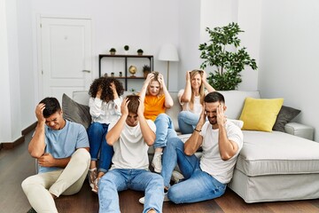 Canvas Print - Group of people sitting on the sofa and floor at home suffering from headache desperate and stressed because pain and migraine. hands on head.