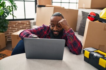 Sticker - Young african american man using laptop sitting on floor at new home