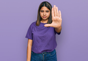 Poster - Young hispanic girl wearing casual purple t shirt doing stop sing with palm of the hand. warning expression with negative and serious gesture on the face.