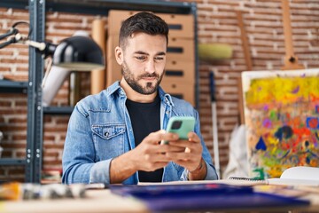 Wall Mural - Young hispanic man using smartphone sitting on table at art studio