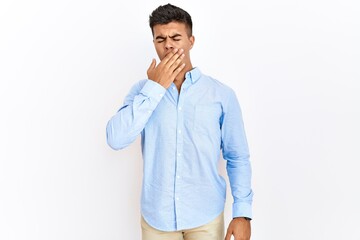 Poster - Young hispanic man wearing business shirt standing over isolated background bored yawning tired covering mouth with hand. restless and sleepiness.