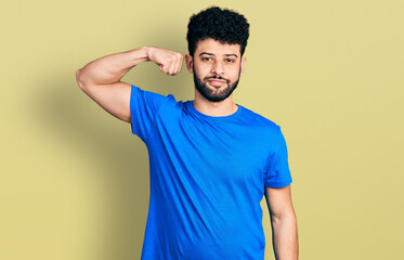 Poster - Young arab man with beard wearing casual blue t shirt strong person showing arm muscle, confident and proud of power