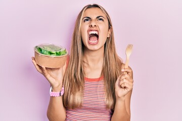 Sticker - Beautiful hispanic woman eating salad angry and mad screaming frustrated and furious, shouting with anger looking up.