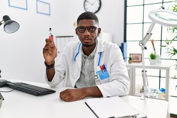 Canvas Print - Young african american doctor man holding electronic cigarette at medical clinic thinking attitude and sober expression looking self confident