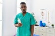 Young african physiotherapist man holding massage body lotion scared and amazed with open mouth for surprise, disbelief face
