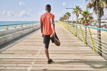 Young african american man wearing sportswear stretching at seaside