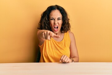 Sticker - Beautiful middle age woman wearing casual clothes sitting on the table pointing displeased and frustrated to the camera, angry and furious with you