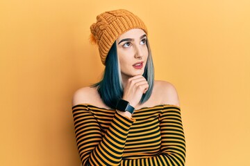 Wall Mural - Young modern girl wearing wool hat with hand on chin thinking about question, pensive expression. smiling with thoughtful face. doubt concept.