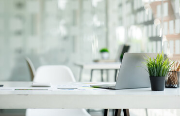Laptop Computer, notebook, and eyeglasses sitting on a desk in a large open plan office space after working hours	

