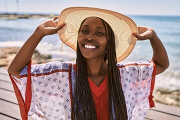 Canvas Print - Young african american woman wearing summer hat standing at the beach.