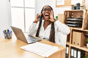 Poster - Black woman with braids working at the office speaking on the phone shouting and screaming loud to side with hand on mouth. communication concept.