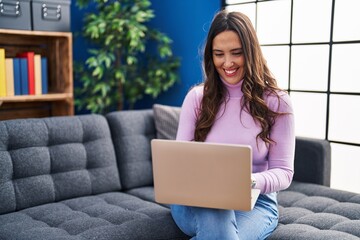 Wall Mural - Young hispanic woman using laptop sitting on sofa at home