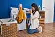 © Krakenimages.com - Young hispanic woman washing clothes smelling dirty towel at laundry room
