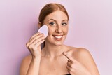 Fototapeta Panele - Young irish woman holding makeup sponge smiling happy pointing with hand and finger
