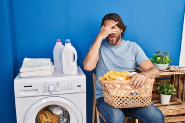 Sticker - Handsome middle age man waiting for laundry peeking in shock covering face and eyes with hand, looking through fingers with embarrassed expression.