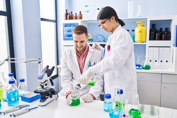 Wall Mural - Man and woman wearing scientists uniform pouring liquid on test tube at laboratory