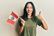Young hispanic girl holding peru flag smiling happy and positive, thumb up doing excellent and approval sign