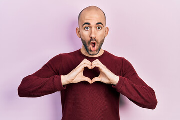 Sticker - Young bald man doing heart symbol with hands afraid and shocked with surprise and amazed expression, fear and excited face.