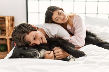 Poster - Young caucasian couple smiling happy lying on the bed playing with dog at home.