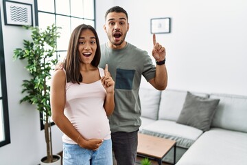 Sticker - Young interracial couple expecting a baby, touching pregnant belly pointing finger up with successful idea. exited and happy. number one.