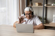 Older man wear headset start videoconference at home. Mature male use laptop greets online therapist, welcoming grownup children living abroad. Distant communication, videocall event, e-health concept