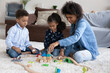 © fizkes - Positive young African mom and two kids playing with toy construction models on soft carpeted floor at home. Teacher, daycare sitter teaching Black little boy and girl to stack blocks, build city road