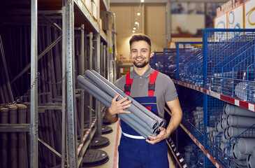 Wall Mural - Happy young man who works as a salesman at the store where you can buy good quality tools and construction materials standing in one of the aisles and holding a bunch of gray PVC U drain pipes