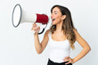 © luismolinero - Young caucasian woman isolated on white background shouting through a megaphone to announce something in lateral position