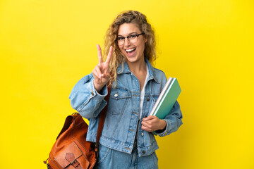 Young student caucasian woman isolated on yellow background smiling and showing victory sign