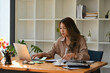 © saltdium - A portrait of a pretty Asian woman sitting in the office looking at a laptop and working on a document, for business and technology concept.