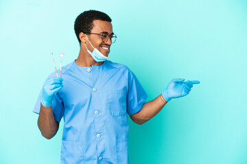 Wall Mural - African American dentist holding tools over isolated blue background pointing finger to the side and presenting a product