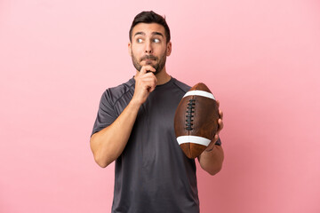 Wall Mural - Young caucasian man playing rugby isolated on pink background having doubts and thinking