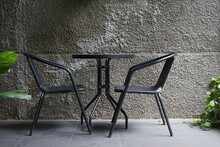 Beautiful And Simple Outdoor Seating With Iron Table And Chair Set. Decoration For Outdoor Cafe With Rough Cement Facade