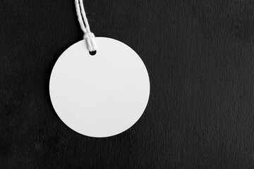 Round white tag label mockup with white cord, close up. Blank paper price tag isolated on black background with copy space, Sale and Black Friday concept