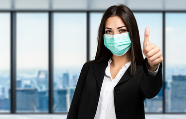 Wall Mural - Smiling businesswoman isolated on white wearing a mask, coronavirus concept, and giving thumbs up