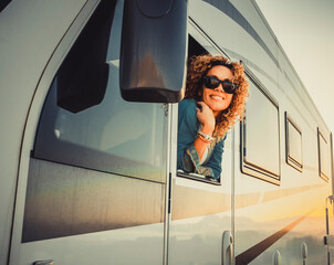 Traveler cheerful and happy expression beautiful young woman outside the driver window of modern camper van mothr home vehicle. Concept of travel and summer holiday vacation and destination people