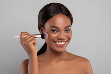 Wall Mural - Closeup Portrait Of Attractive Happy Black Female Using Blusher Brush