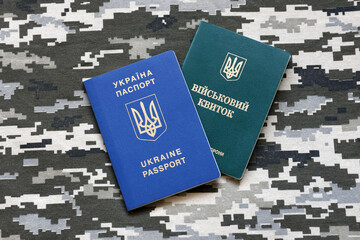 Wall Mural - Ukrainian military ID and foreign passport on fabric with texture of pixeled camouflage. Cloth with camo pattern in grey, brown and green shapes with Ukrainian army personal token and passport.