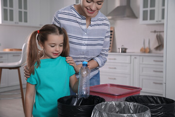 Sticker - Young woman and her daughter throwing plastic bottle into trash bin in kitchen. Separate waste collection