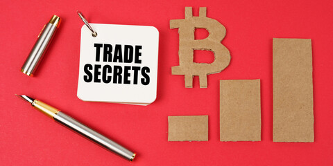 Poster - On a red surface lie the bitcoin symbol, a pen and a notepad with the inscription - TRADE SECRETS